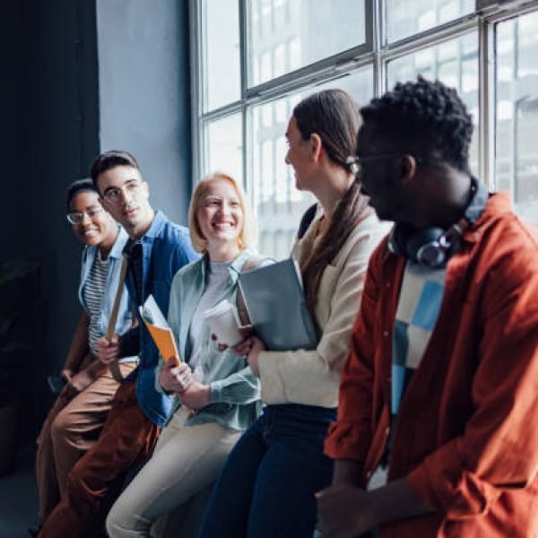 Smiling multi ethnic group of friends standing in a row and leaning on a window while talking and laughing together.